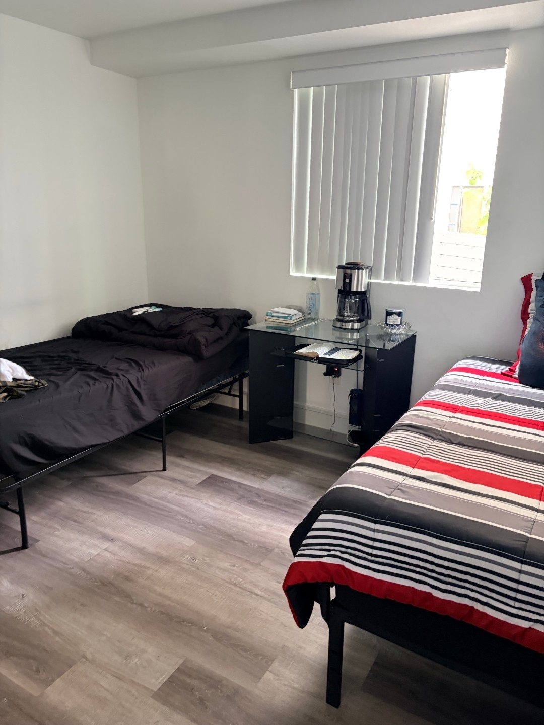 A clean, furnished Aim High Living room with two beds, a desk, and natural light